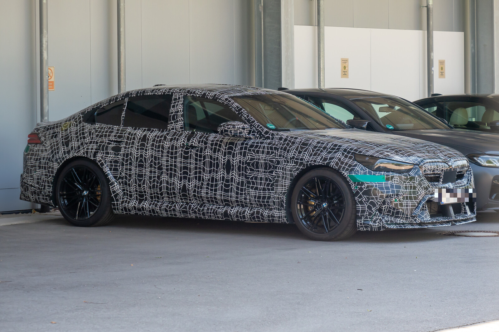 Ein getarnter BMW M5 G90 als Testfahrzeug steht in M�nchen auf einem Parkplatz, aufgenommen schr�g von vorn. Das Foto entstand am 21. Juli 2024.