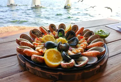 Meeresfrüchteplatte in einem bretonischen Küstenrestaurant: Arrangement aus Austern, Krabben, Hummer und Miesmuscheln mit Vinaigrette und Zitronenscheiben auf rustikalem Holztisch vor Meereskulisse.