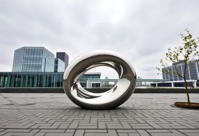 Abstrakte Stahlskulptur in urbaner Umgebung mit reflektierenden Oberflächen und moderner Architektur im Hintergrund