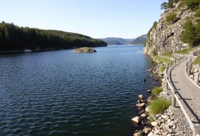 Stausee inmitten von Wäldern mit Felswand und Wanderpfad am Ufer